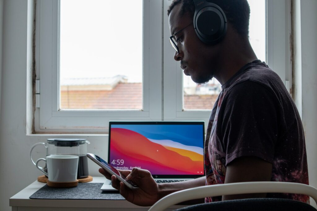 Person looking at their phone using the best work from home wireless headphones with their laptop on their desk next to some coffee.