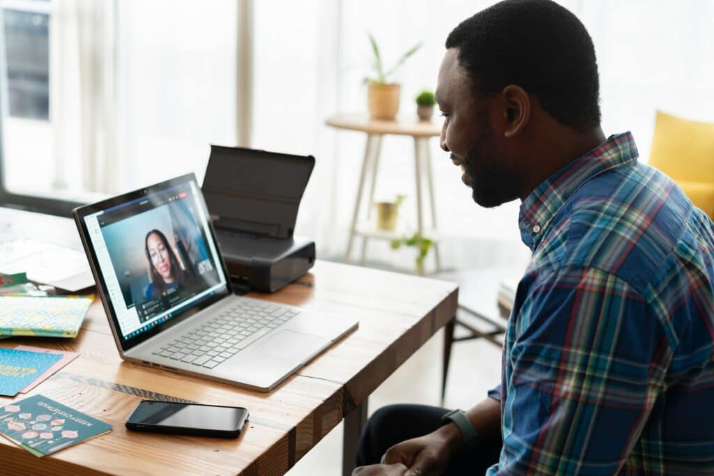 A person sat on their kitchen table on a zoom call on their laptop while working from home.