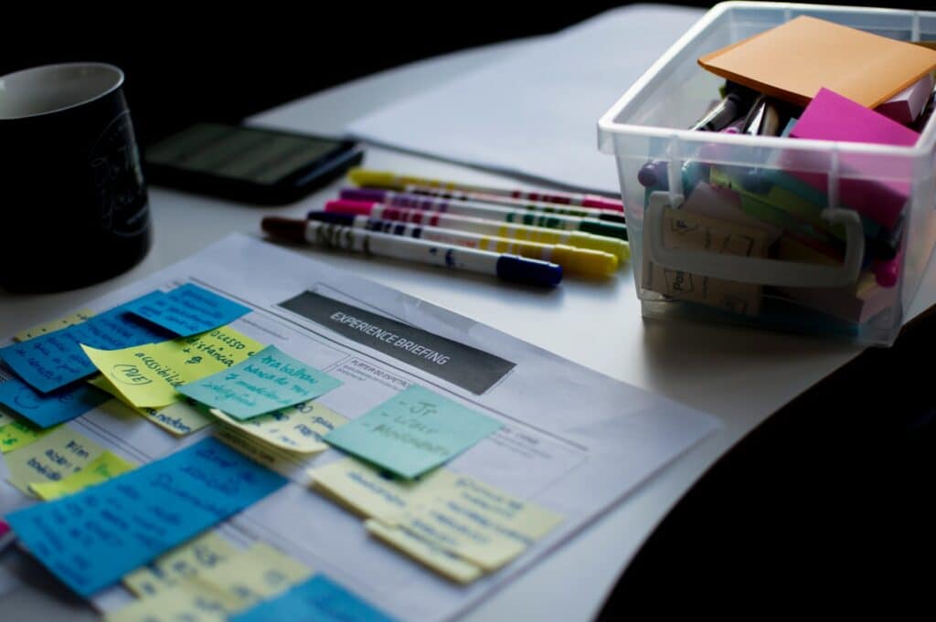 Getting yourself prepared to make the perfect pitch deck is important! Here we have someone making notes on paper on a desk with pens and post-it notes.